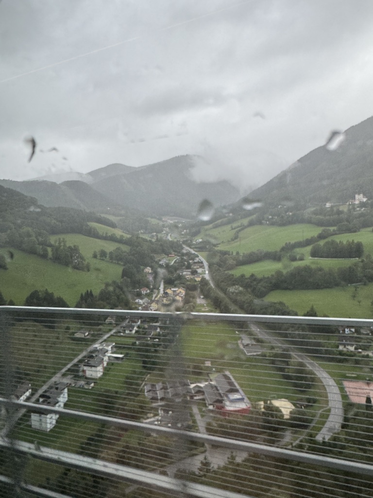 A view of a valley from a high bridge through a rain covered bus window